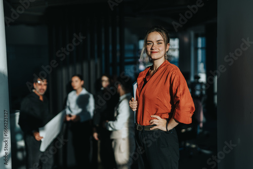 Photography A confident woman in a red blouse stands in a modern office, leading a team meeting
