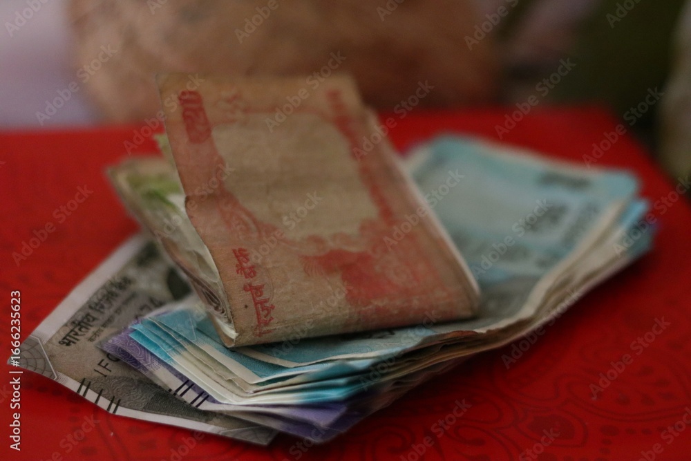 Obraz premium Stacked and folded Indian rupee notes on a red background, used as a sacred offering during worship, puja ceremonies, and cultural traditions.