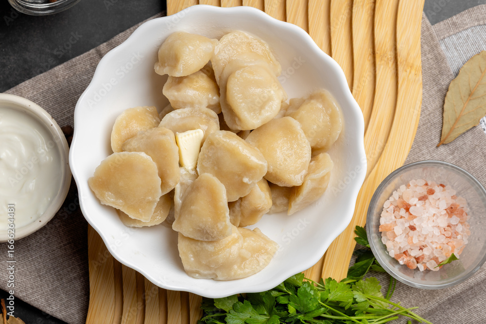 Fototapeta premium Freshly cooked dumplings pelmeni in rustic plate, topped with greenery and pepper, authentic Eastern European homemade food.