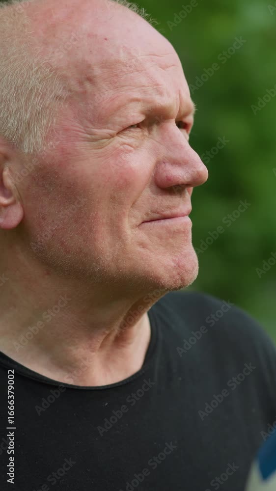 An elderly man rolls a soccer ball in his hand with a focused expression, with a blur view of trees and other equipment in the background An elderly man rolls a soccer ball in his hand with a focused expression, with a blur view of trees and other equipment in the background