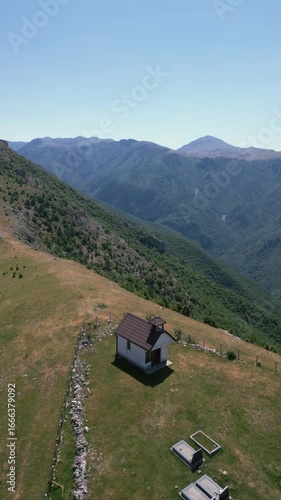 Aerial drone view of a rocky mountain ridge with scattered vegetation and clear blue sky, representing natural landscape and wilderness.