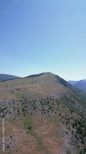 Aerial drone view of a rocky mountain ridge with scattered vegetation and clear blue sky, representing natural landscape and wilderness.