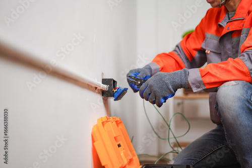 Electrician working on electrical outlet installation and maintenance in modern residential home with professional tools and safety gear