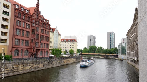 Berlin, Germany - June 1, 2025: Scenic view of Nikolaiviertel in Berlin featuring two riverboats cruising along the Spree River, surrounded by historic buildings and greenery.