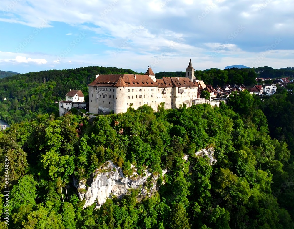 Obraz premium Panoramic view of a medieval castle perched atop a hill, surrounded by lush greenery and a valley below