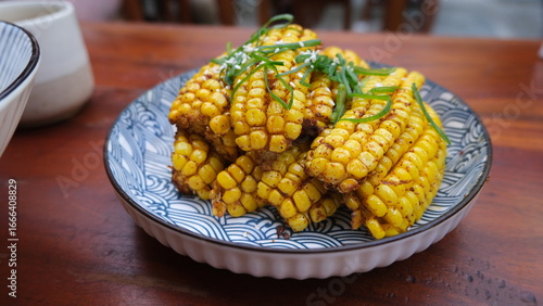Obraz na plátně Golden fried corn ribs cut into small sections and garnished with herbs, served on a decorative ceramic plate over a wooden table