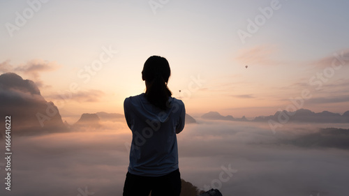 Person watching sunrise over foggy mountains in peaceful outdoor setting  at  Phadeng Peak, Luang Prabang, Laos