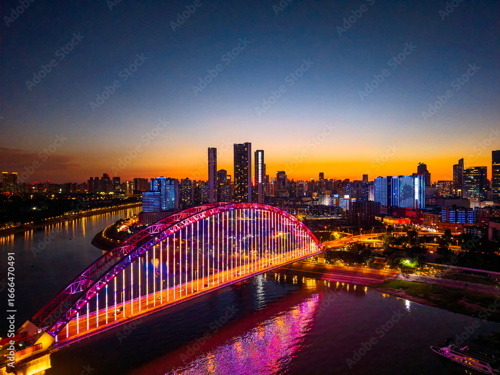 Fototapeta premium Wuhan China cityscape showcases a beautifully illuminated bridge crossing the Yangtze River, with its vibrant lights reflecting on the water, shining brightly under the twilight sky.