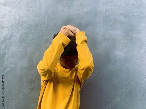A young male teenager cowers, protecting his head with his hands, a powerful image representing the fear and pain of a bullying victim