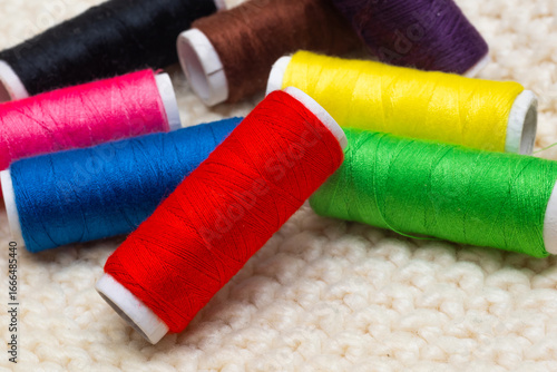 A set of colored threads for sewing on spools. A stack of multi-colored spools of thread