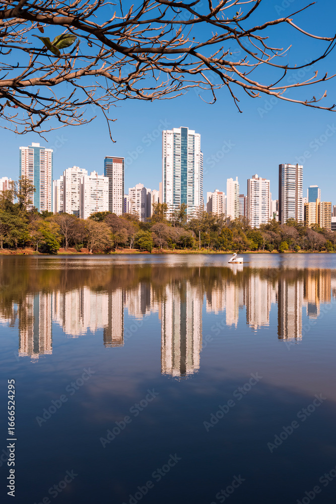 Fototapeta premium Urban view of the city of Londrina, Brazil, with a lake in the foreground, a strip of vegetation in the middle, and residential skyscrapers in the background.