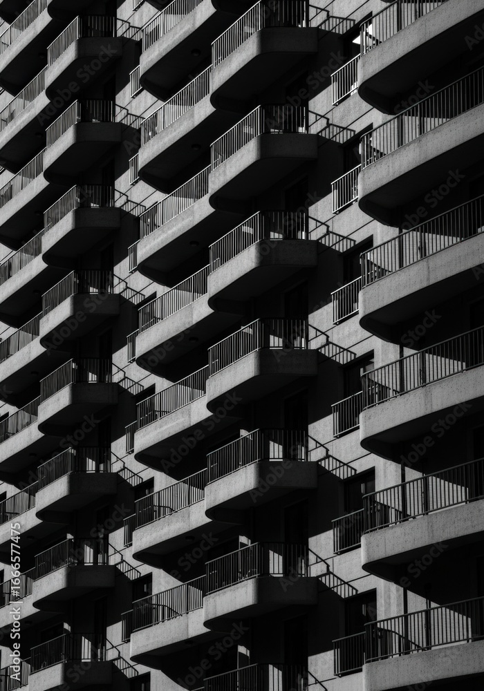 Obraz premium Close-up view of modern high-rise apartment building with repetitive balcony design and metal railings in black and white photography