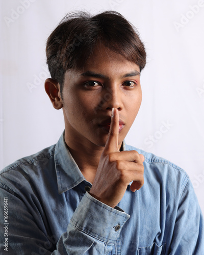 Foto Portrait of Asian man in blue shirt making shushing gesture, asking to be quiet, silence concept