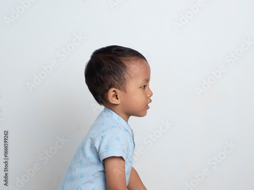 Konstfotografi Asian toddler wearing blue patterned shirt standing facing sideways on white isolated background