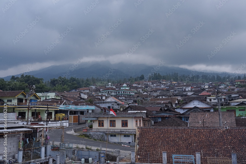 Obraz premium Sunday, August 3, 2025, 14:20:52, Temanggung, Indonesia _ Misty Mountain Village A Scenic View of Houses nestled beneath Cloudy Peaks