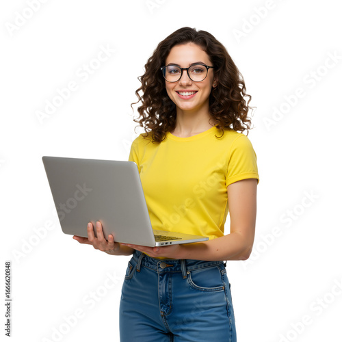 This high-resolution image features a young woman with curly brown hair and glasses, wearing a bright yellow T-shirt and blue jeans, holding a silver laptop with both hands. Her friendly smile and con