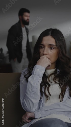Hopeless young woman sitting on sofa while her husband screaming. Domestic violence, people, abuse