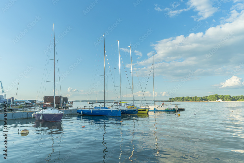 Obraz premium Sailboats docked at quiet marina under clear blue sky. Yachts moored quietly in the harbor, poised for new journeys beneath an endless sky of freedom and possibility.