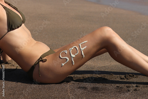 SPF inscription on woman's leg made with sunscreen. Close-up of applying sunscreen to skin. SPF protection. Beach vacation. Safe tanning. Sea vacation, sunbathing on the beach