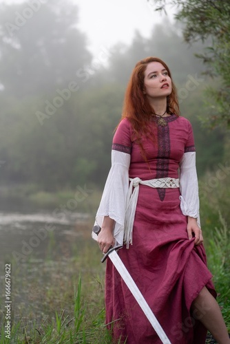 Foto Redhead warrior gazes skyward, sword in hand, amidst misty reeds and water