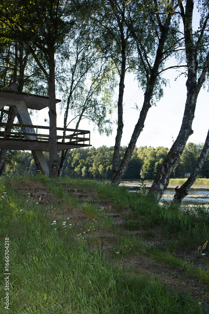 Fototapeta premium geometric concrete tower with concrete steps leading up to it against the backdrop of a river and forest