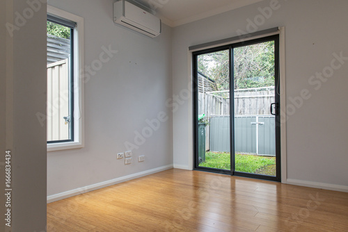 Minimalist modern interior with bamboo flooring, light gray walls, and a glass sliding door opening to a small fenced backyard with green grass
