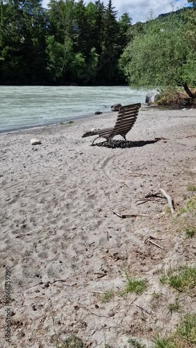 Peaceful outdoor relaxation spot by a turquoise river with sand, driftwood, trees, and soothing water sounds.