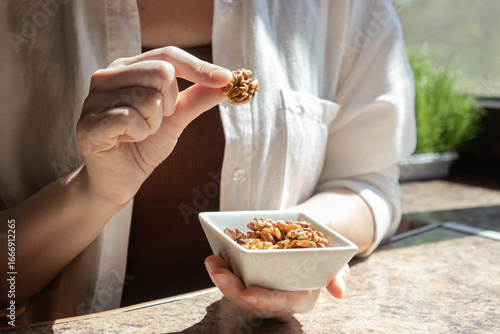 Close up of woman taking walnut from small bowl with shelled walnuts. Concept of brain food, omega-3 nutrition and healthy snack.