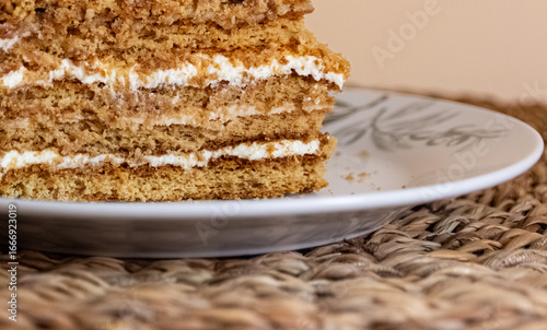 Piece of cake (medovnik) is on a plate. Layered cake, with crumbs around it. Served on a white plate on a wooden place mat. Closeup photograph. Version 2.