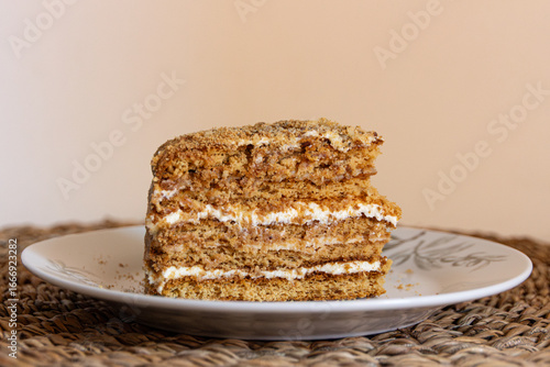 Piece of cake (medovnik) is on a plate. Layered cake, with crumbs around it. Served on a white plate on a wooden place mat. Closeup photograph. Version 3.