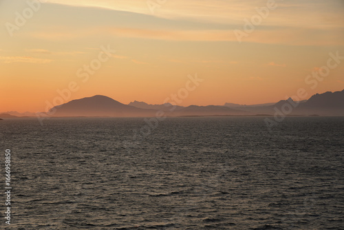 Der Sonnenaufgang vor der Küste Norwegens taucht den Himmel in wundervolle Farben und lässt die Berge mystisch aussehen