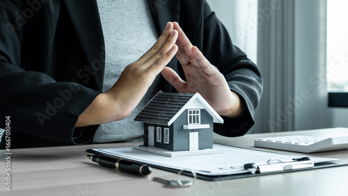 Real estate agent covering Small house model and protection by hands
