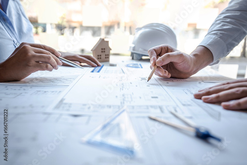 Team of architects or engineering consulting and analyzing working on objects tools and construction drawings inspection, discussing planning new architectural project on blueprint and model house