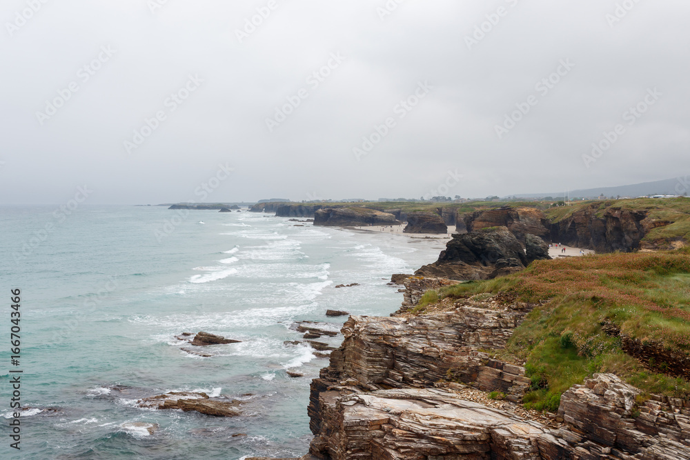 Obraz premium Turists visiting Cathedrals beach playa de las catedrales Spain Atlantic ocean. Natural rock arch on Cathedrals beach in low tide Cantabric coast, Lugo Galicia