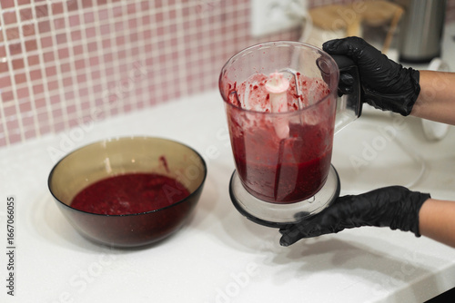 Close-up of a woman's gloved hands cooking berry jam made from fresh raspberries in the kitchen