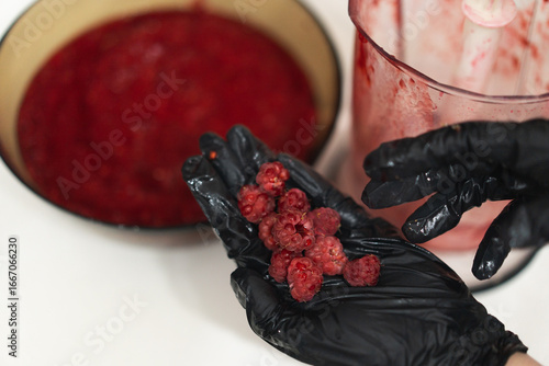 Close-up of a woman's gloved hands cooking berry jam made from fresh raspberries in the kitchen