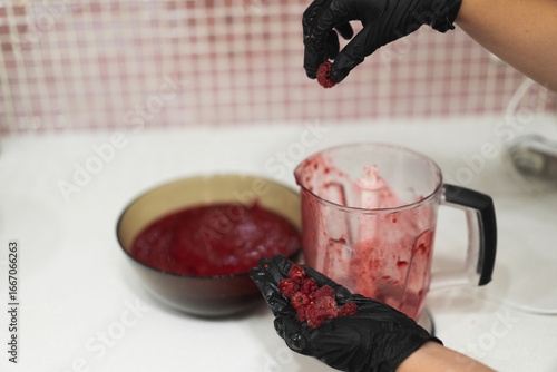 Close-up of a woman's gloved hands cooking berry jam made from fresh raspberries in the kitchen
