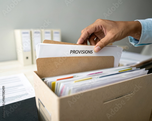 Hand placing document labeled provisions into file folder organized office workspace business management paperwork professional efficient calm atmosphere close up