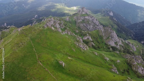 Aerial drone footage of green hills and rocky formations in the Ciucas Mountains, Romania. Captured on a clear day, showcasing natural landscapes and dramatic mountain scenery