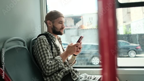 Young man sitting on a bus seat, using smartphone while commuting. Passenger traveling in public transport with modern technology. Horizontal 4k slow motion footage