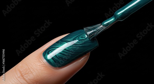 Closeup of a finger with a green marble nail polish application with a brush poised above the nail