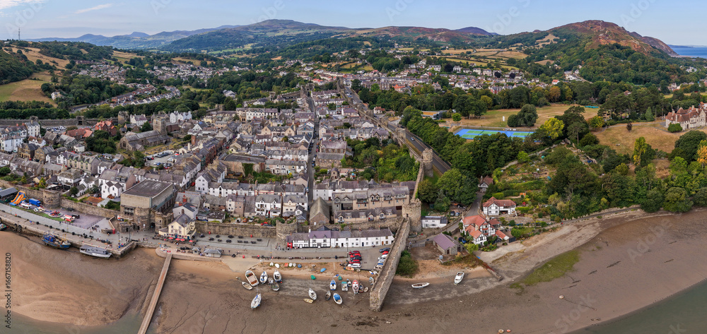 Fototapeta premium Aerial view of Conwy, Wales, showing the historic town walls, waterfront, and surrounding countryside summer skies.