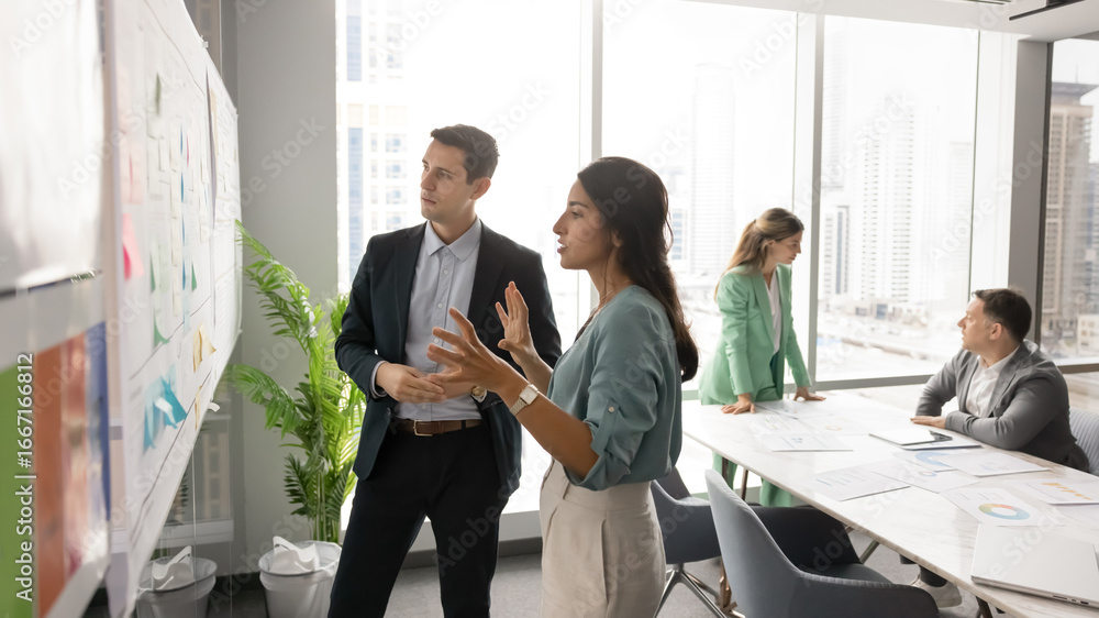 Αυτοκόλλητο In modern office with city view, woman and man standing near whiteboard filled w