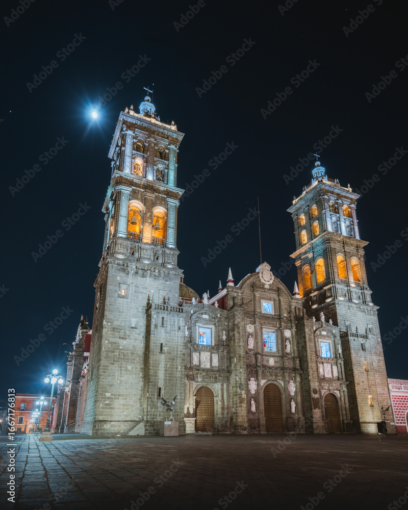 Fototapeta premium Catedral de Puebla iluminada de noche con la luna al fondo, arquitectura histórica y patrimonio cultural de México en un ambiente nocturno espectacular.