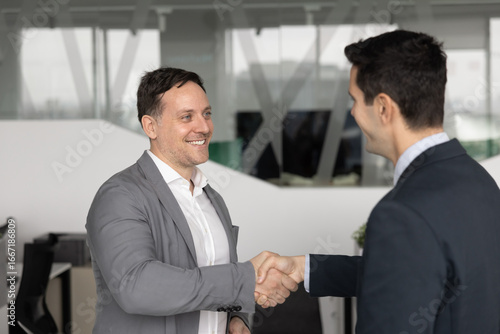 Wallpaper Mural Two smiling businessmen dressed in suits standing in office, shaking hands, as gesture of mutual agreement, successful negotiation accomplishment, start professional collaboration. Trust, partnership Torontodigital.ca