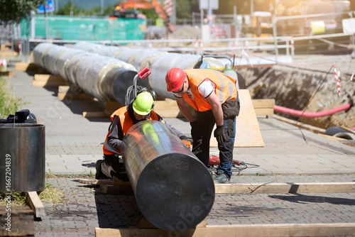 Workers installing pre-insulated district heating pipeline at an urban construction site. Ideal for: energy infrastructure projects, public utility visuals, and civil engineering documentation.