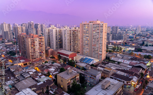 Skyline of Santiago, Chile at sunset with modern skyscrapers, historic buildings, and the Andes mountains in the distance, viewed from Cerro Santa Lucía with lush greenery in the foreground.