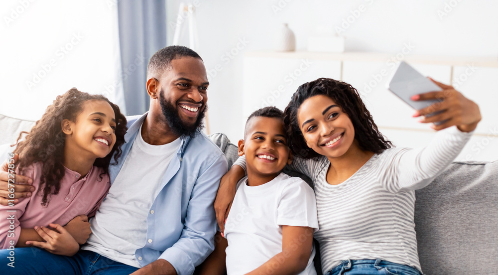 Obraz premium Bonding And Lifestyle. Portrait of african american family taking selfie together at home indoors. Happy parents posing with their children and smiling at camera, sitting on the couch in living room