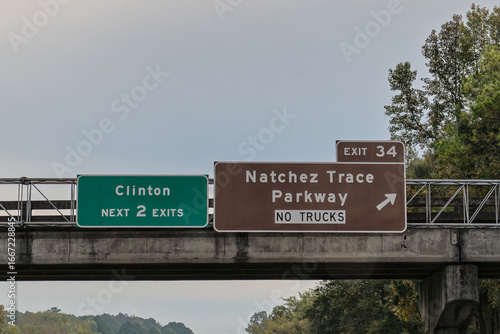 Exit signs on I-20 in Clinton, Mississippi for Exit 34 to Natchez Trace Parkway. Brown signs indicate tourist oriented destinations with recreational, cultural or historical significance