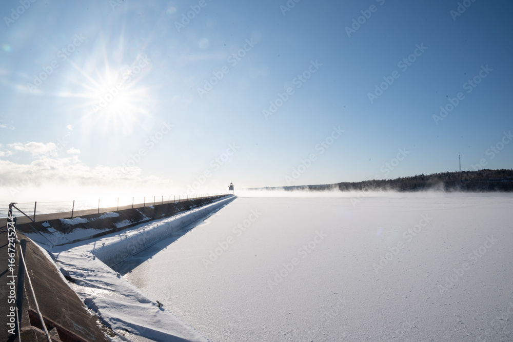 Obraz premium Snow-covered pier leading to lighthouse on frozen Lake Superior